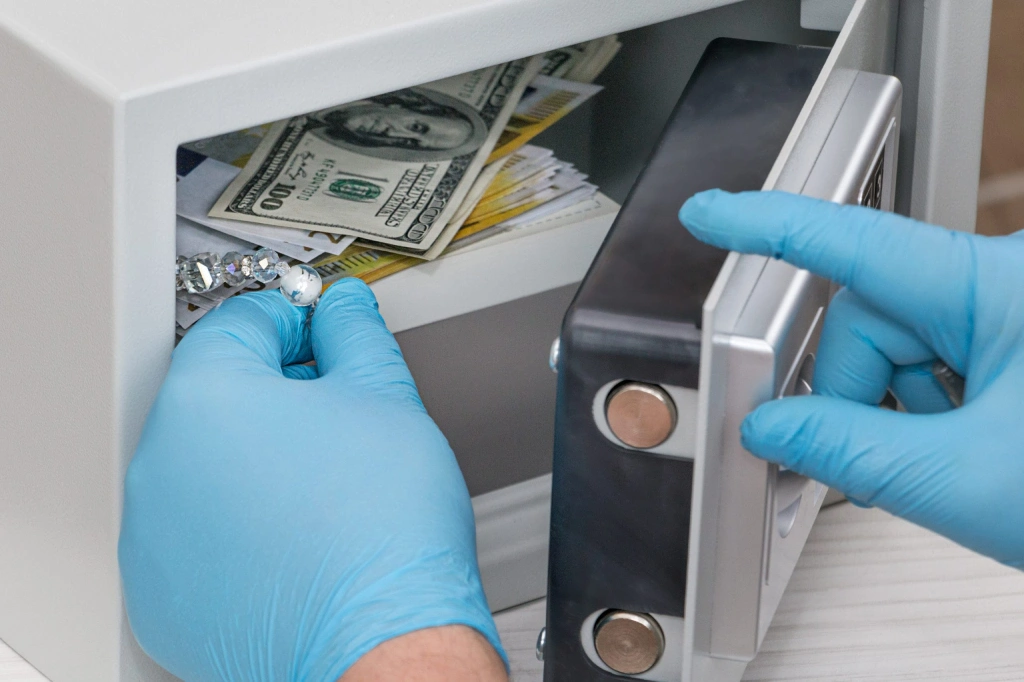 Hands in blue gloves putting jewelry and money into a small safe.