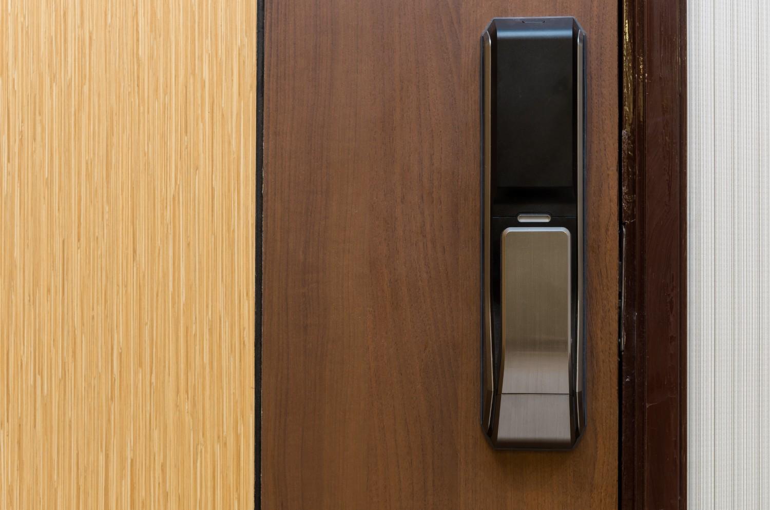 Close-up of a modern black digital door lock on a wooden door.