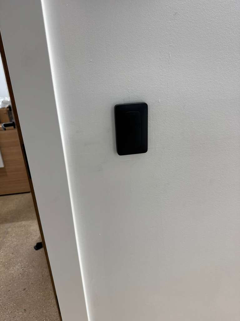 Black rectangular device mounted on a white wall next to a doorway