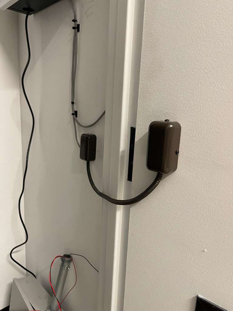Door sensor with wires on a white wall and door frame.
