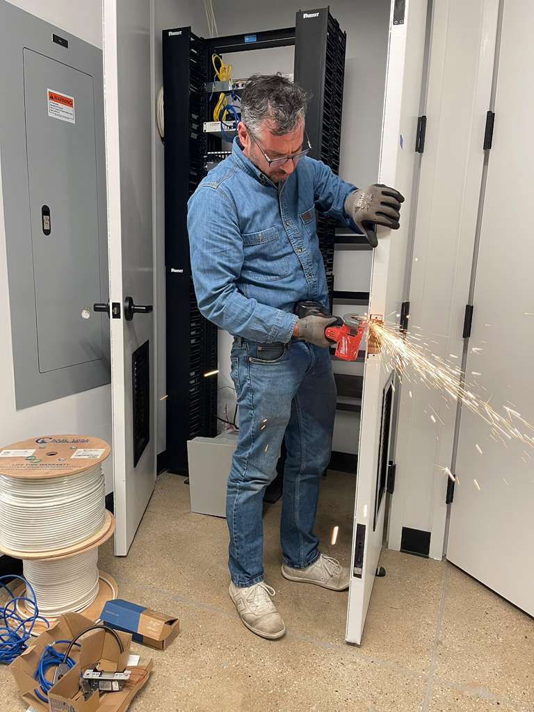 Man cutting metal with sparks flying in a server room.