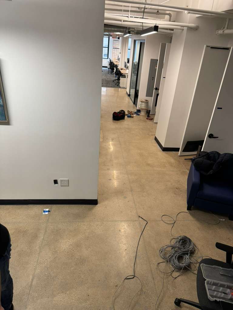 Office hallway with exposed concrete floor, white walls, and scattered items.