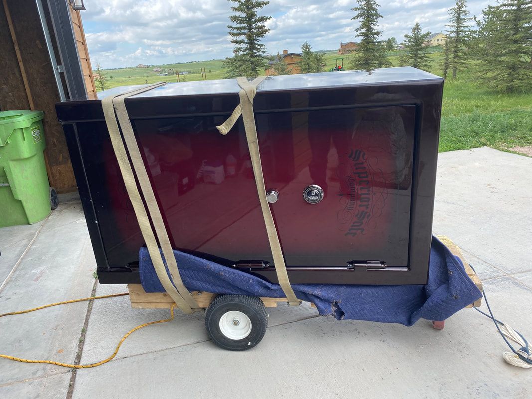 Large dark red and black safe strapped to a wooden cart with small wheels.
