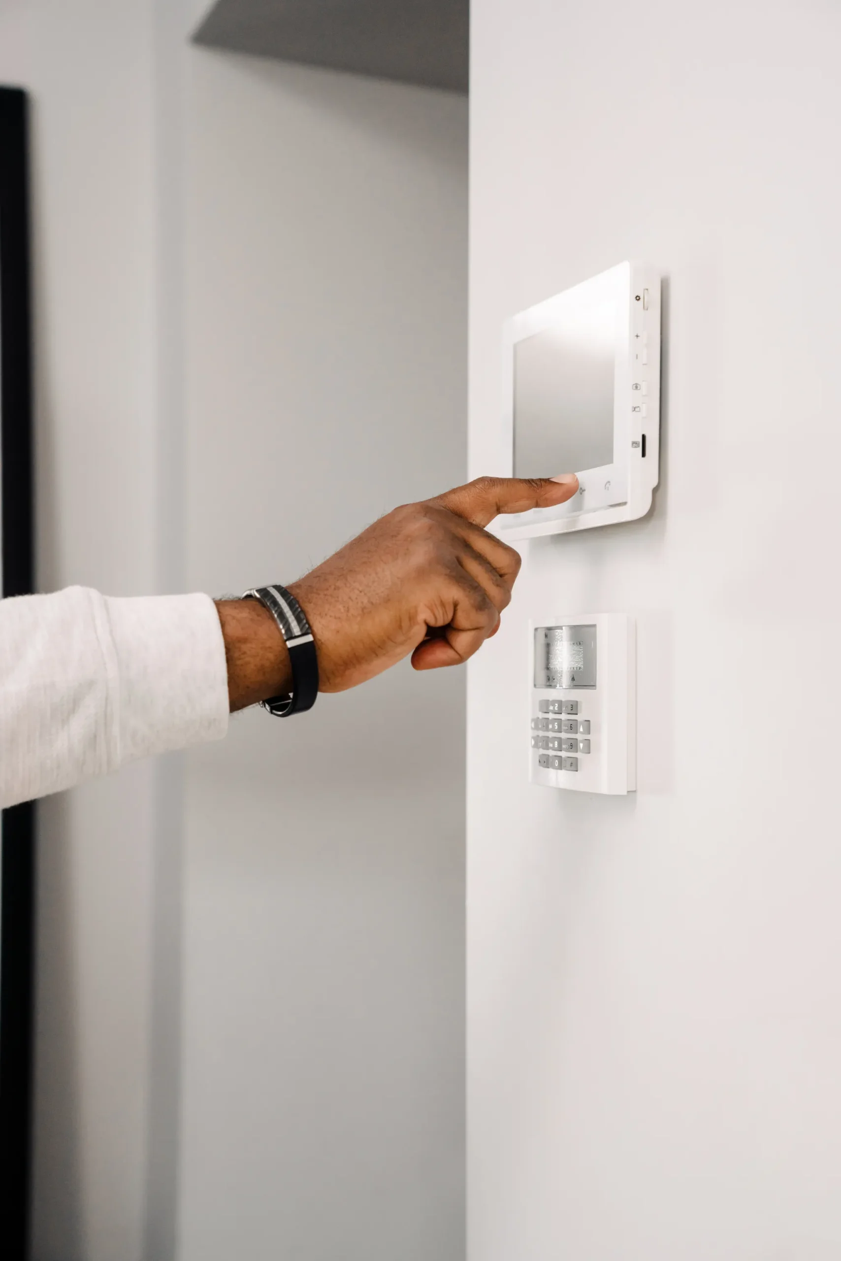 A hand pressing a button on a white smart home control panel.