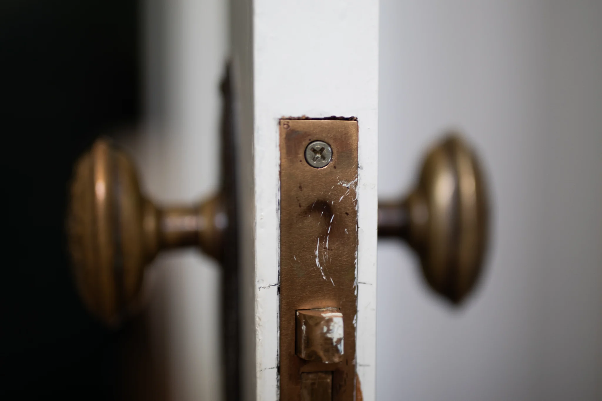 Close-up of an old brass door handle and latch plate on a white door.