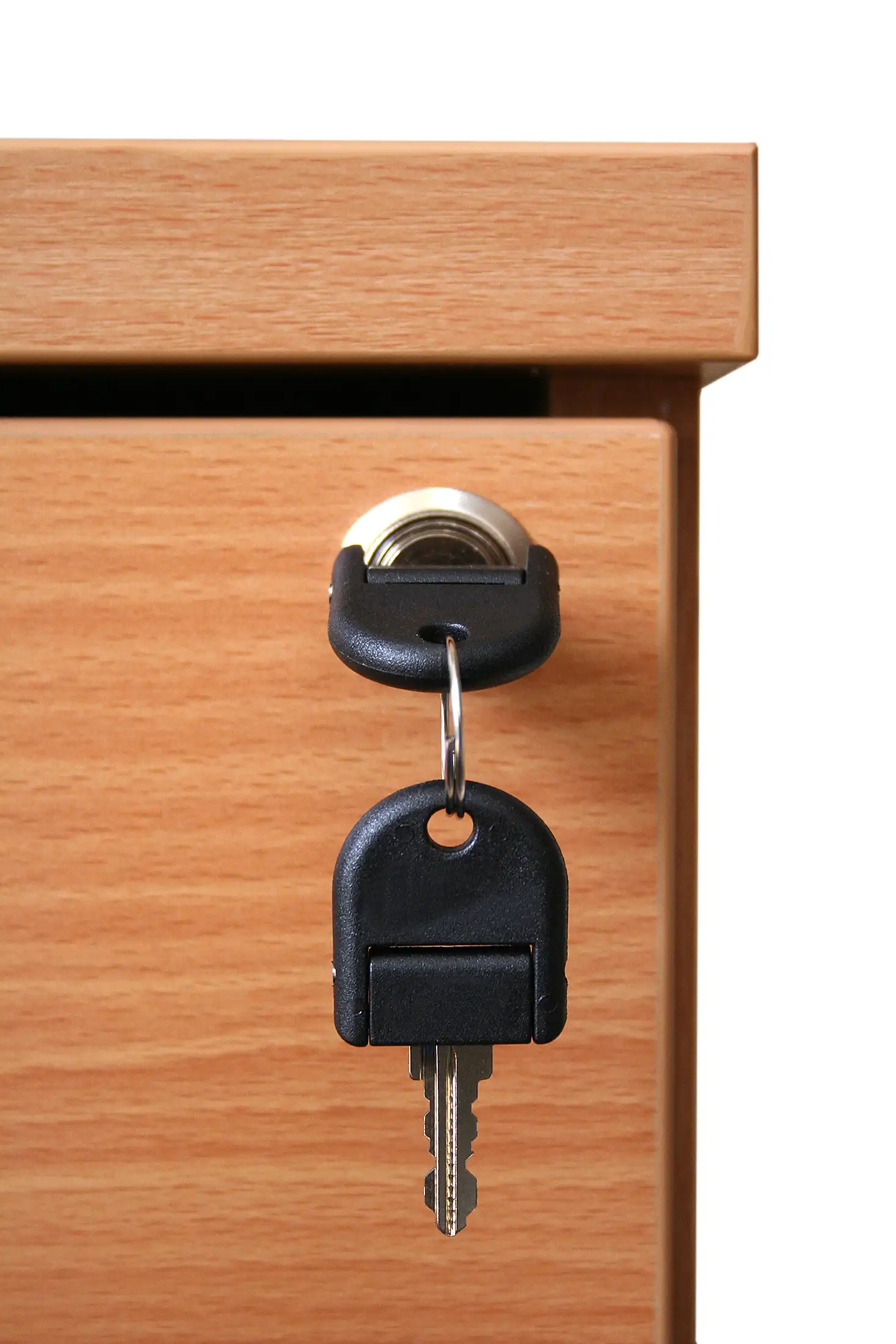Two black keys in a lock on a light brown wooden drawer.