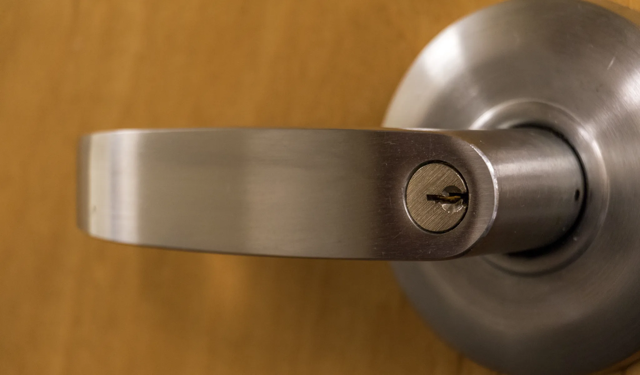Close-up of a silver door handle with a keyhole on a wooden door.