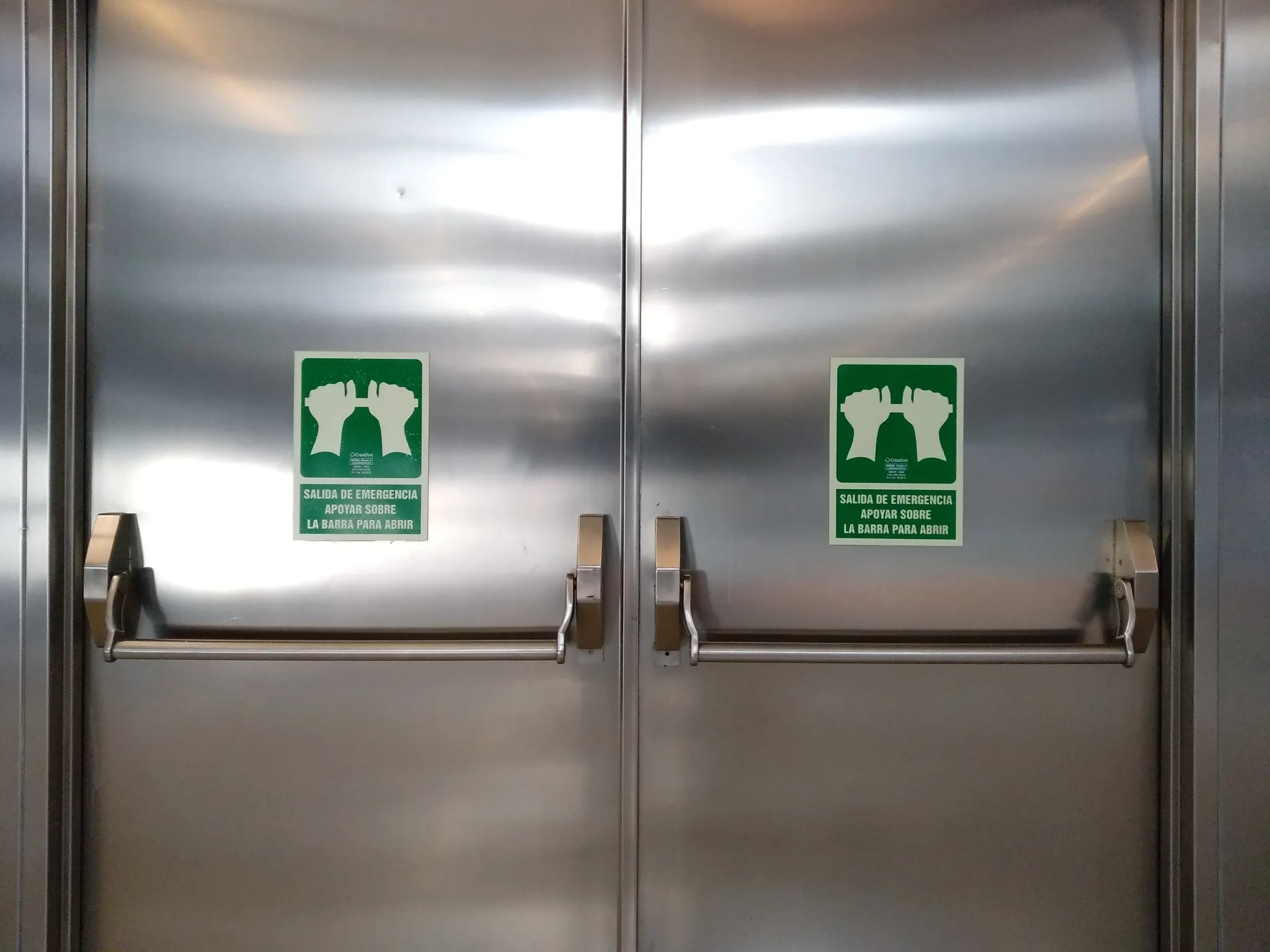 Two silver emergency exit doors with green push bar signs