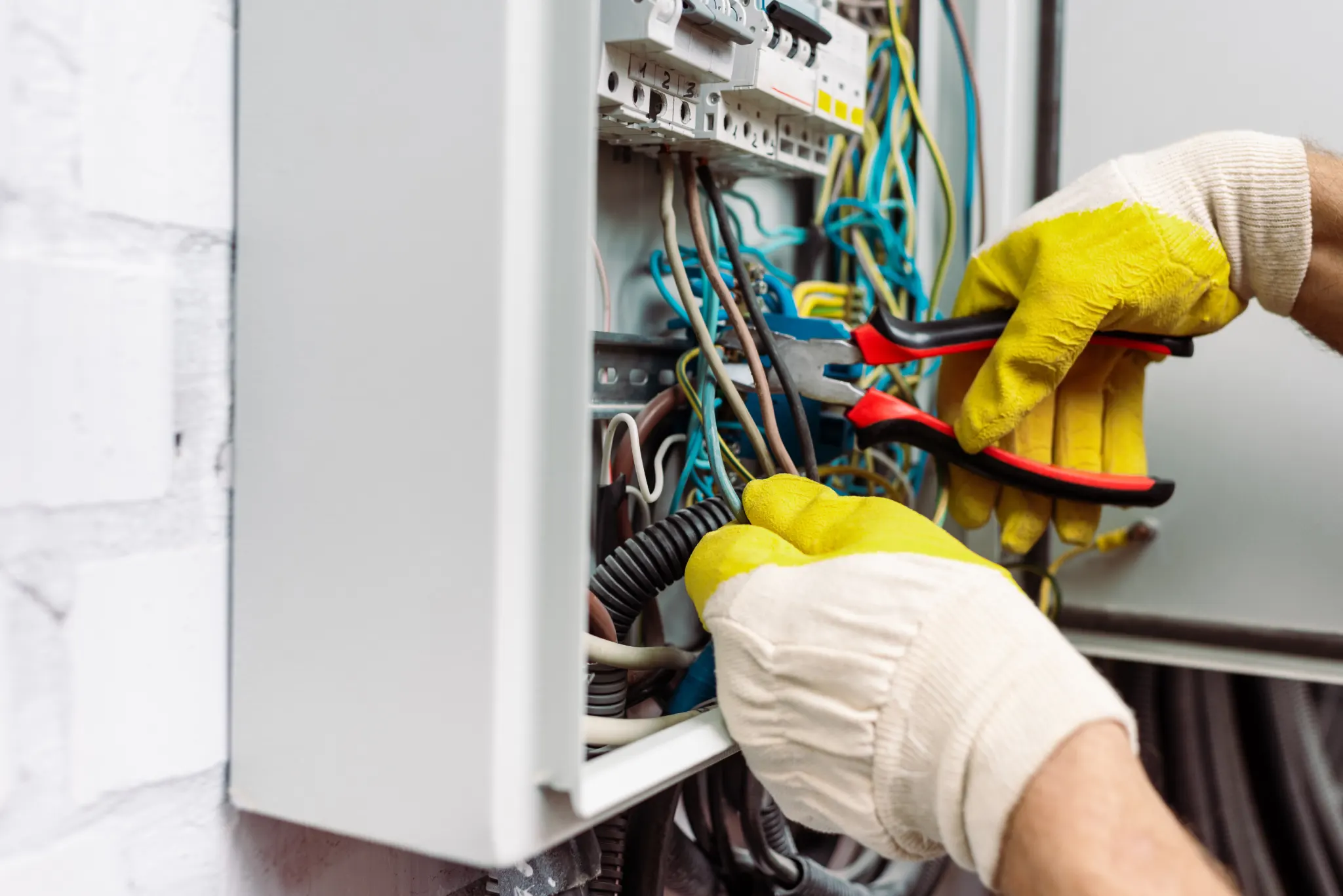 Hands in yellow gloves working on an open electrical panel with wires.