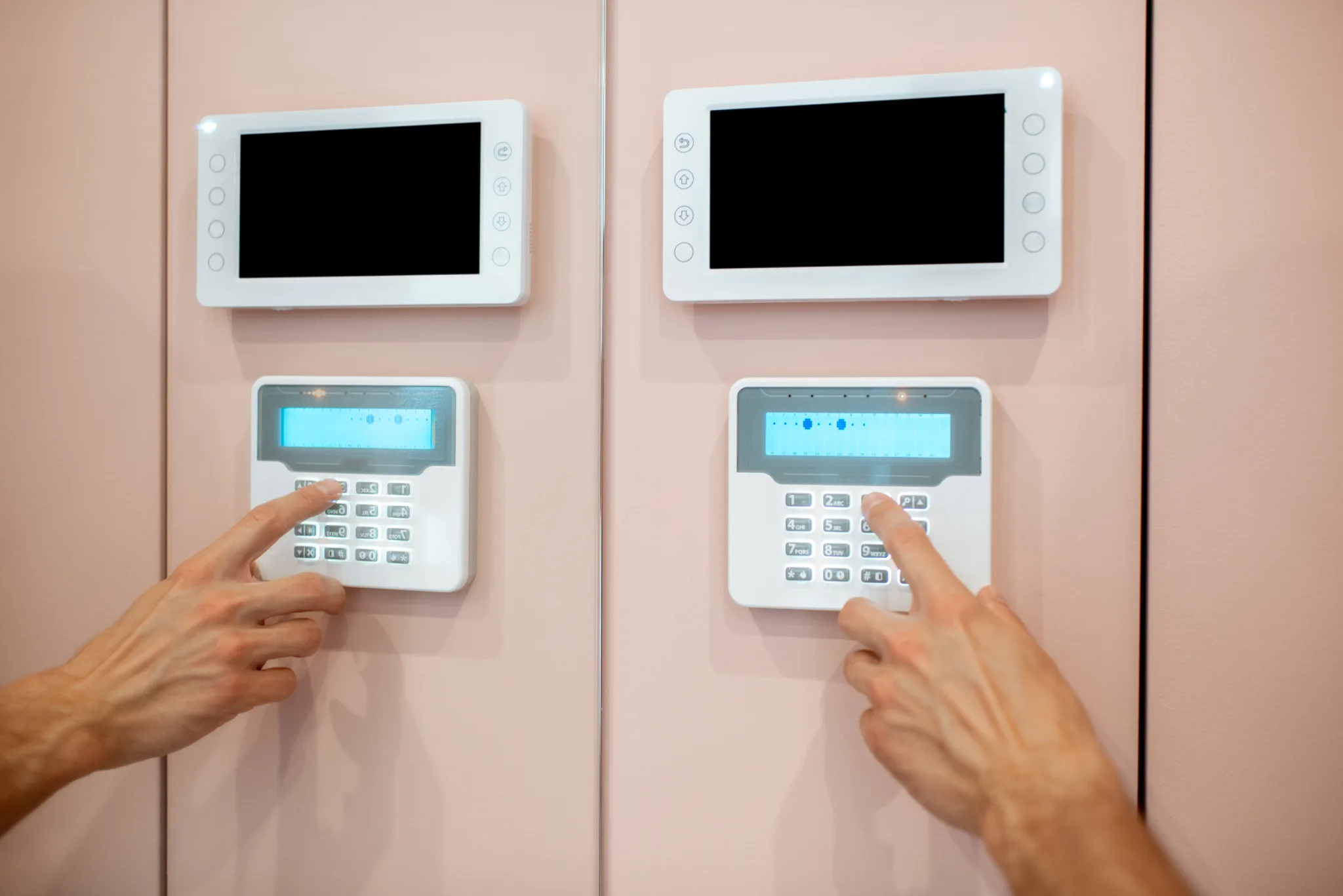 Two hands operating two identical white security keypads with screens.