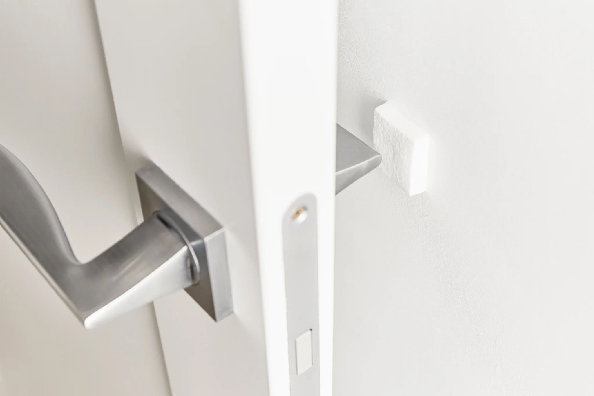 Close-up of a white door with a silver handle and a white wall protector.