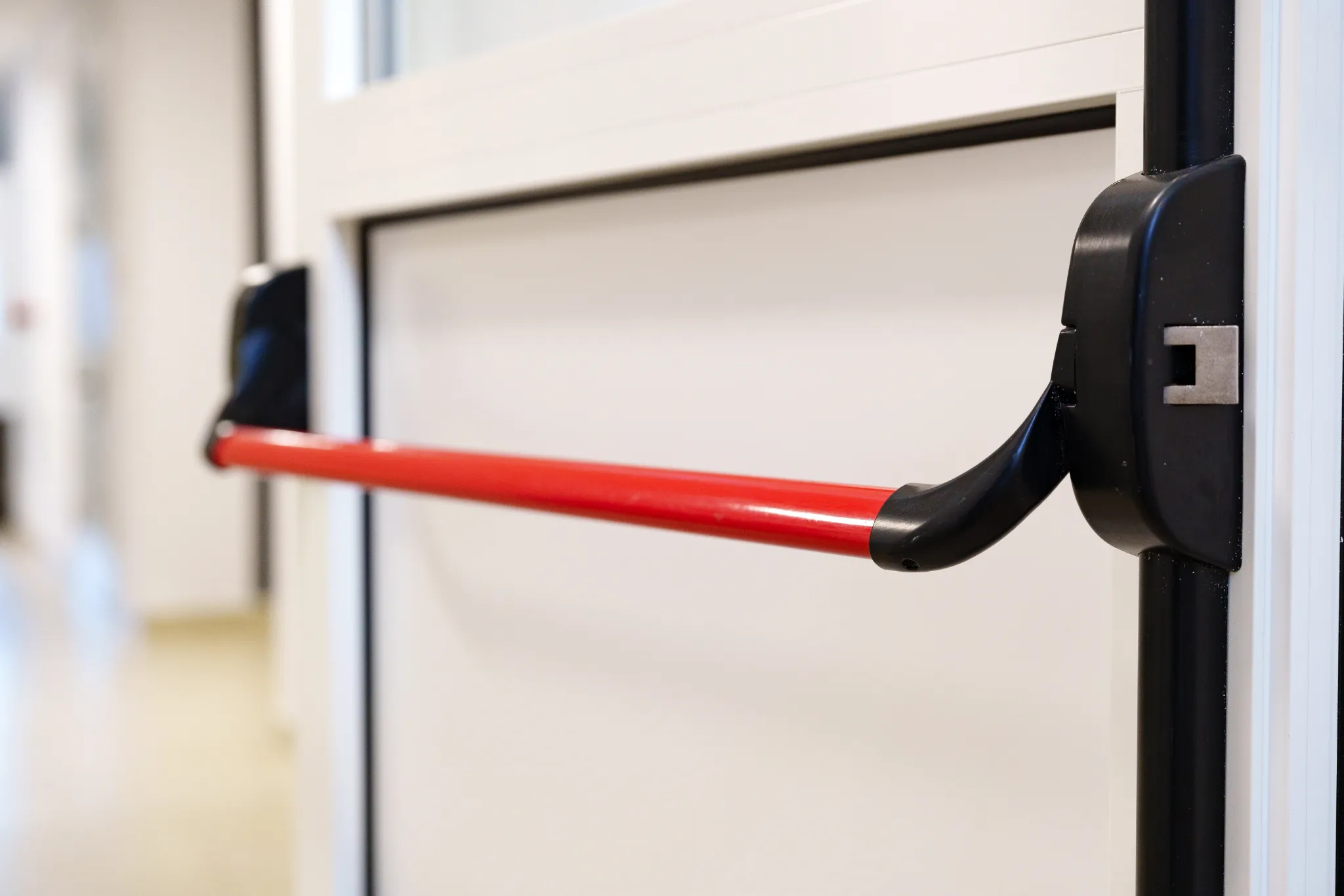 Close-up of a red push bar on a white emergency exit door.