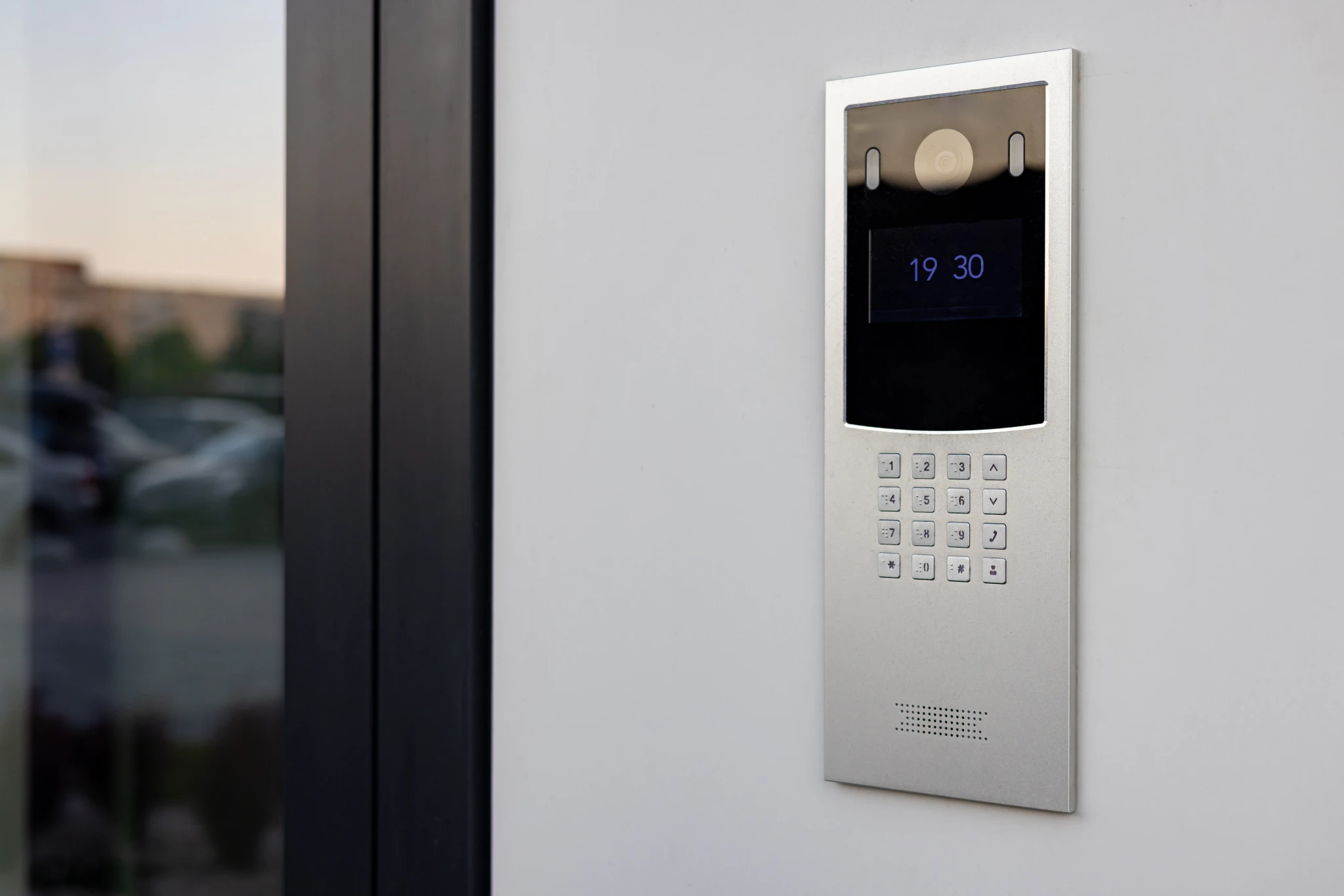 Silver intercom with digital display showing 19:30 on a white wall
