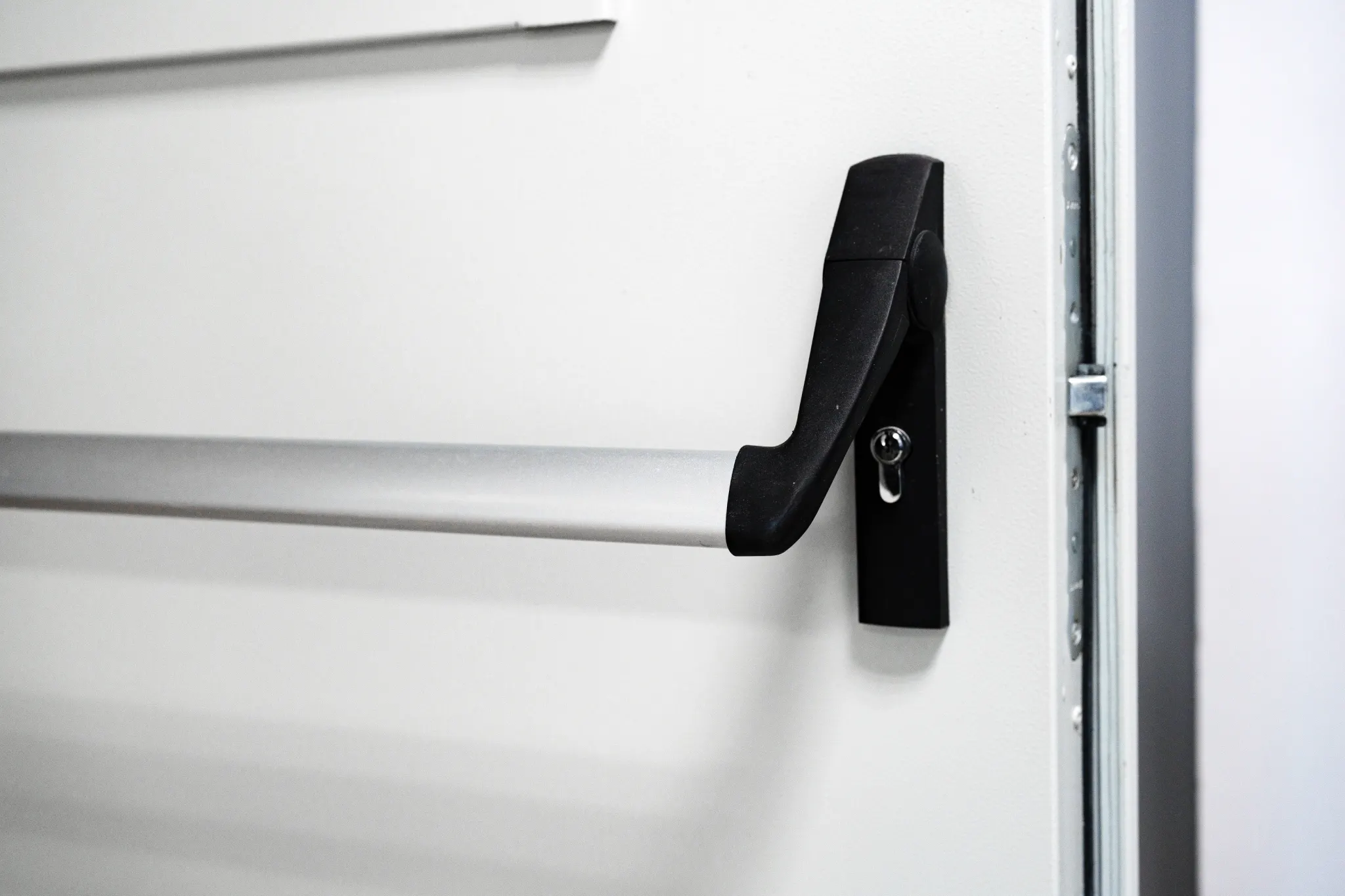 Close-up of a silver and black panic bar on a white door