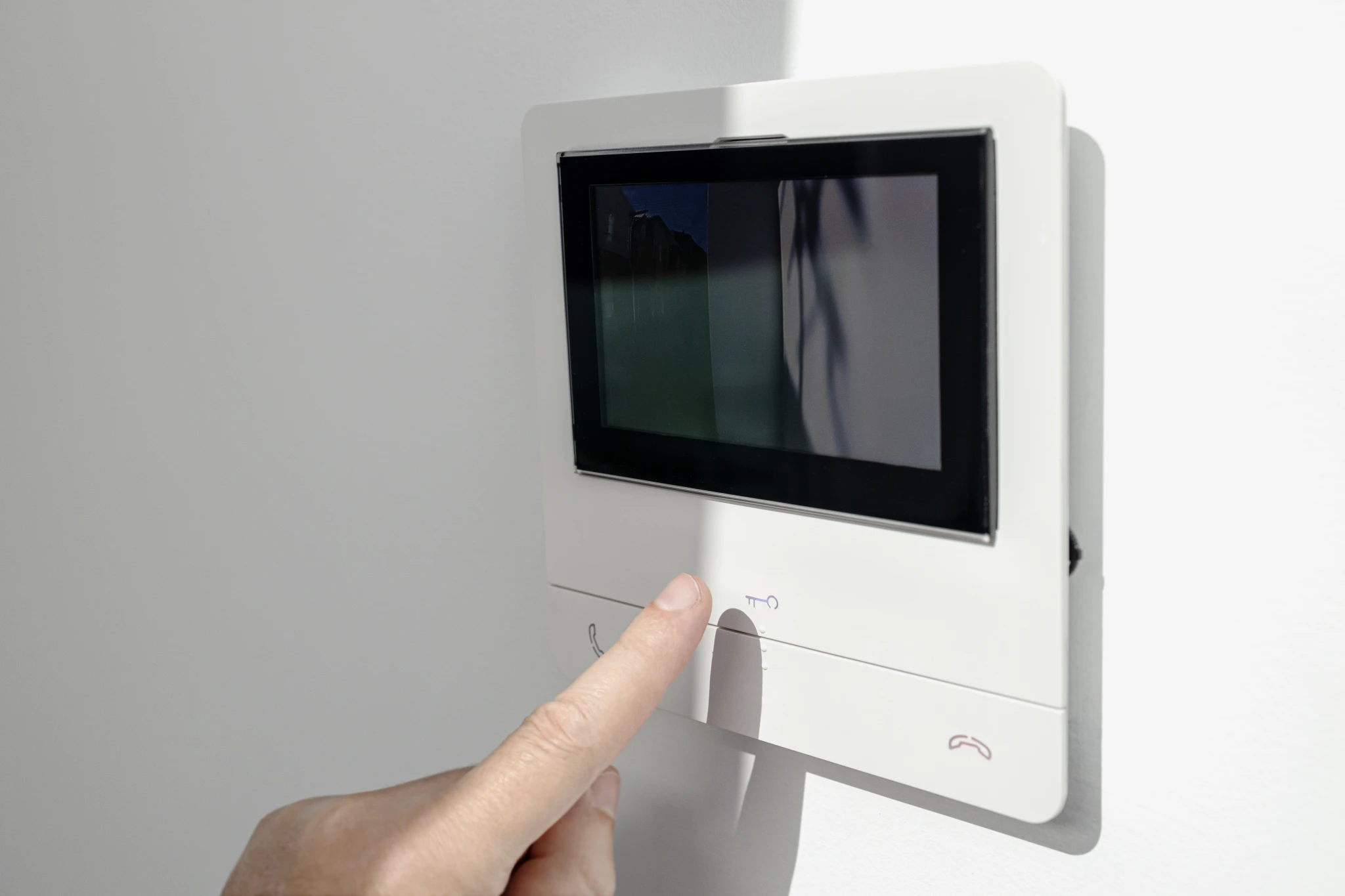 Finger pressing a button on a white video intercom system