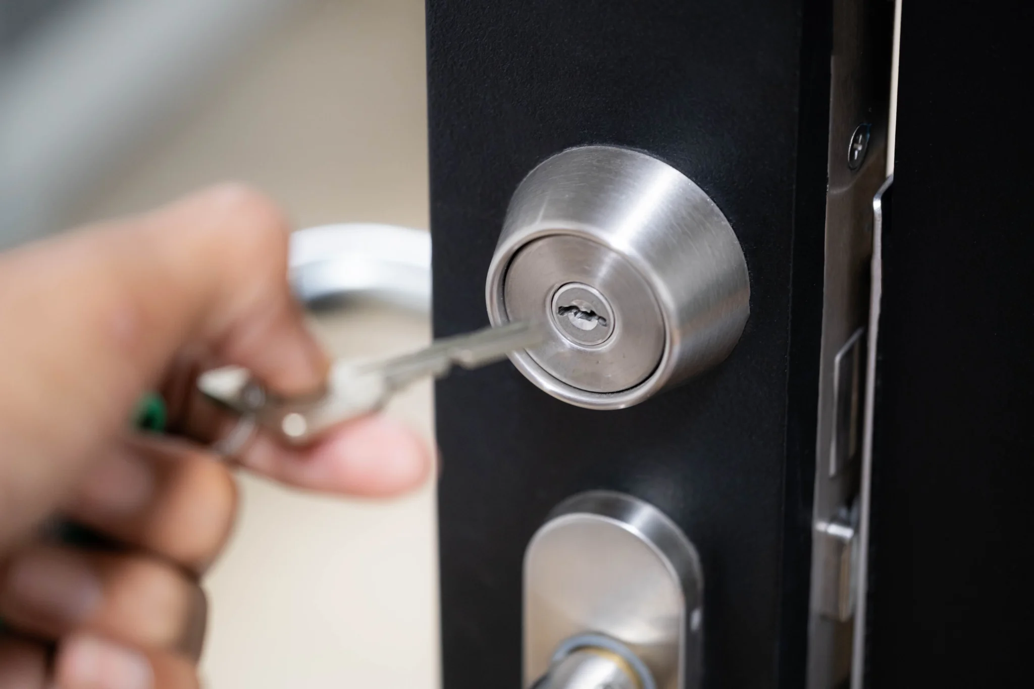 Close-up of a hand inserting a key into a silver door lock.