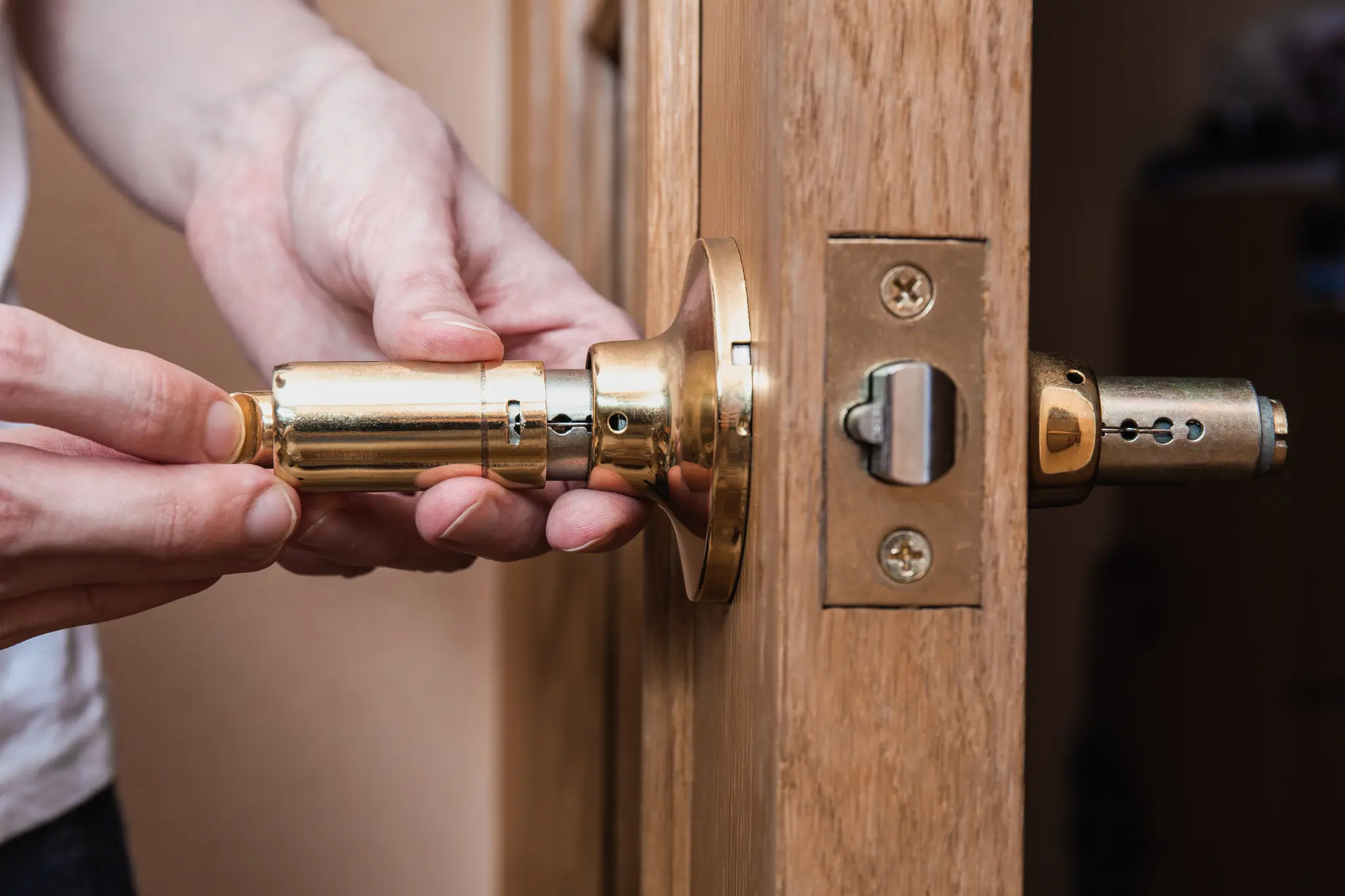 Hands installing a gold door handle into a wooden door.