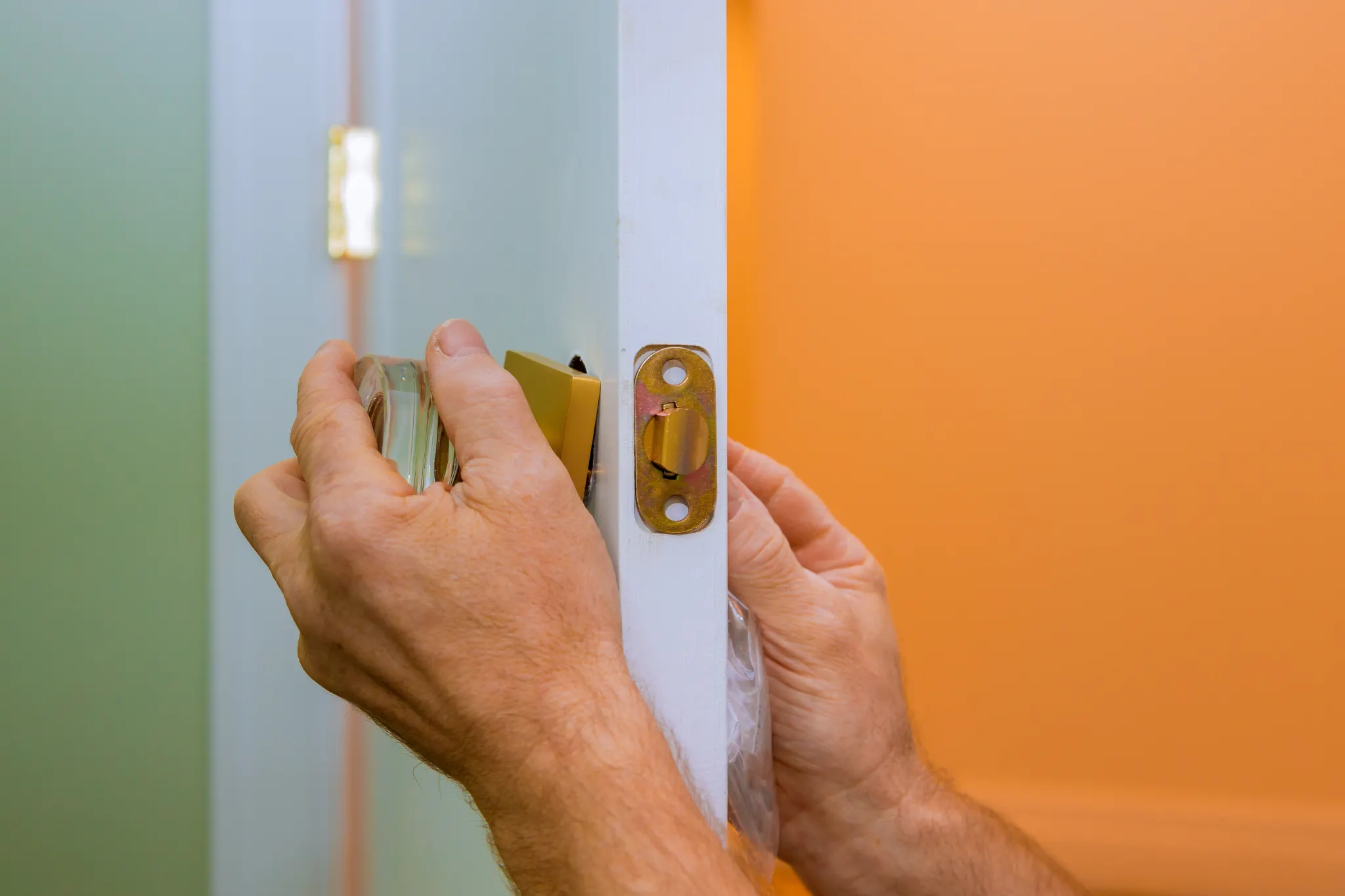 Hands installing a doorknob on a white door frame