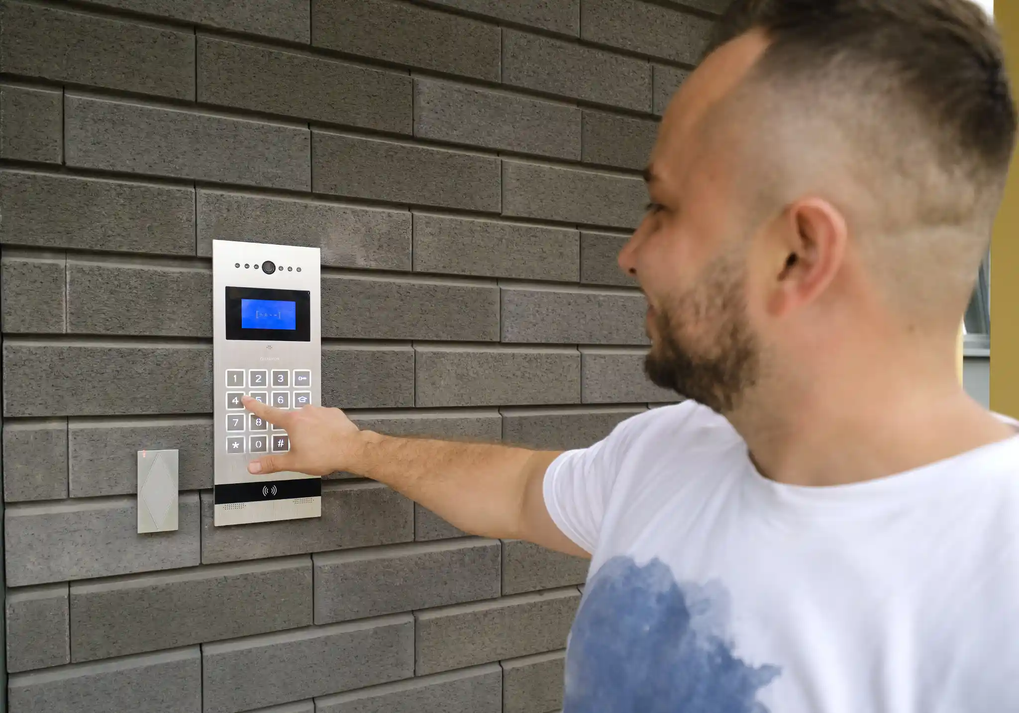 Man's hand pressing a button on a modern intercom system.