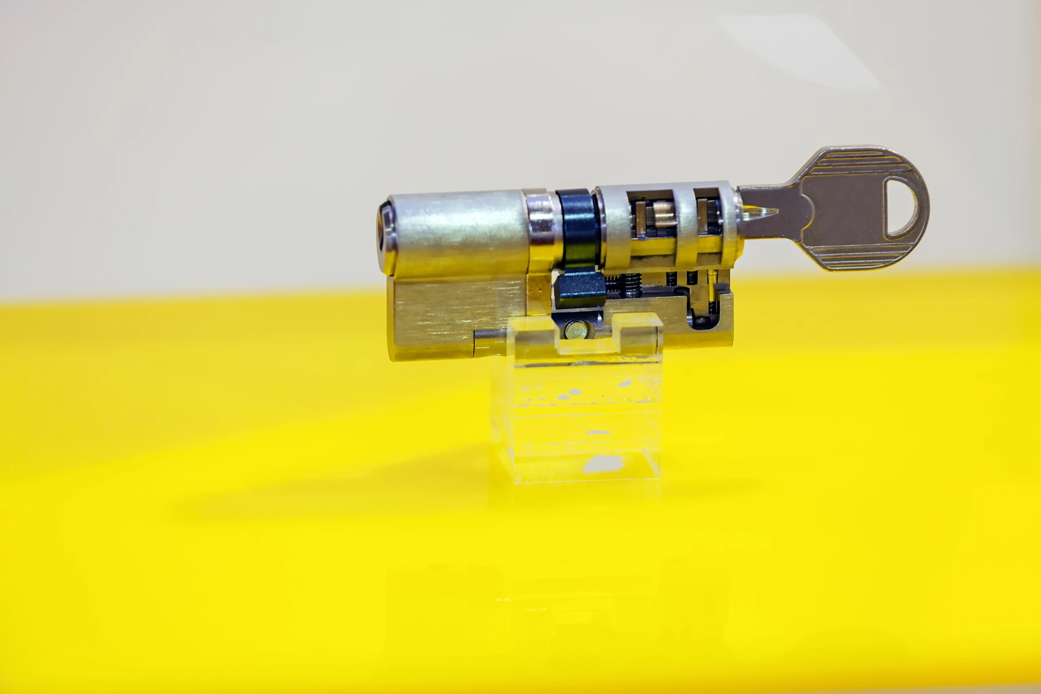 Cutaway view of a cylinder lock with a key inserted, on a yellow surface.