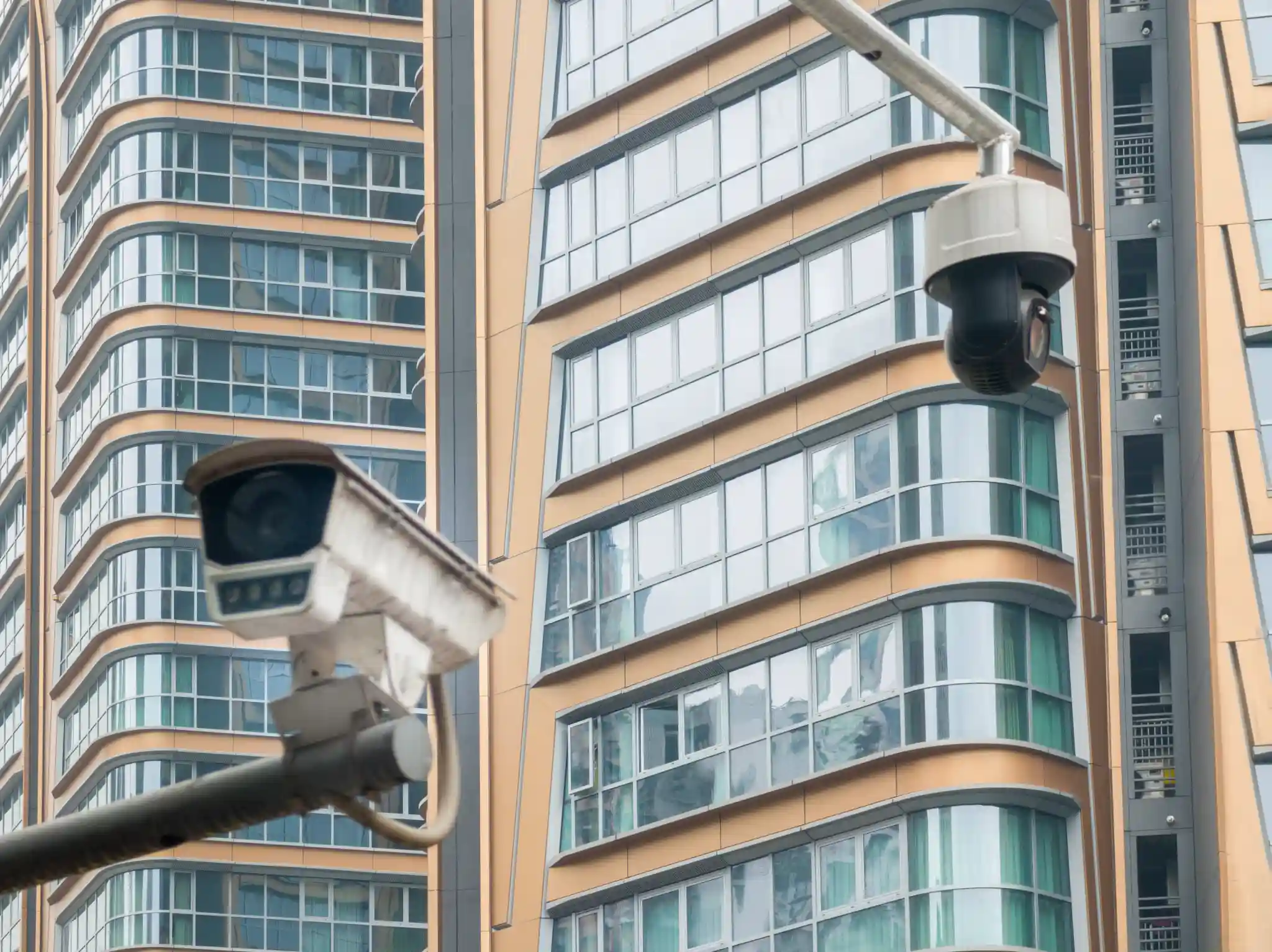 Two security cameras mounted on poles in front of modern buildings
