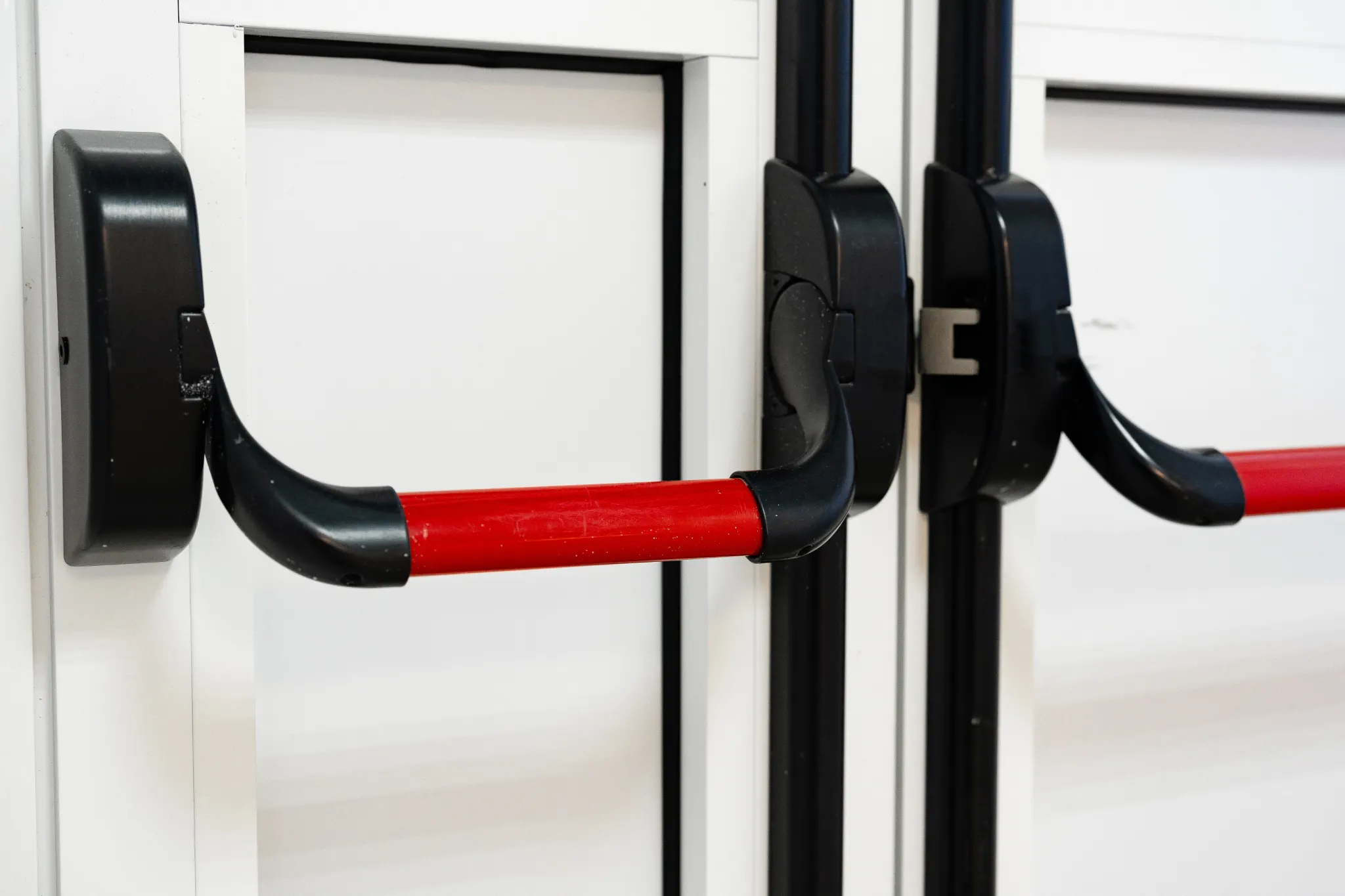 Close-up of two red and black emergency exit push bars on white doors.