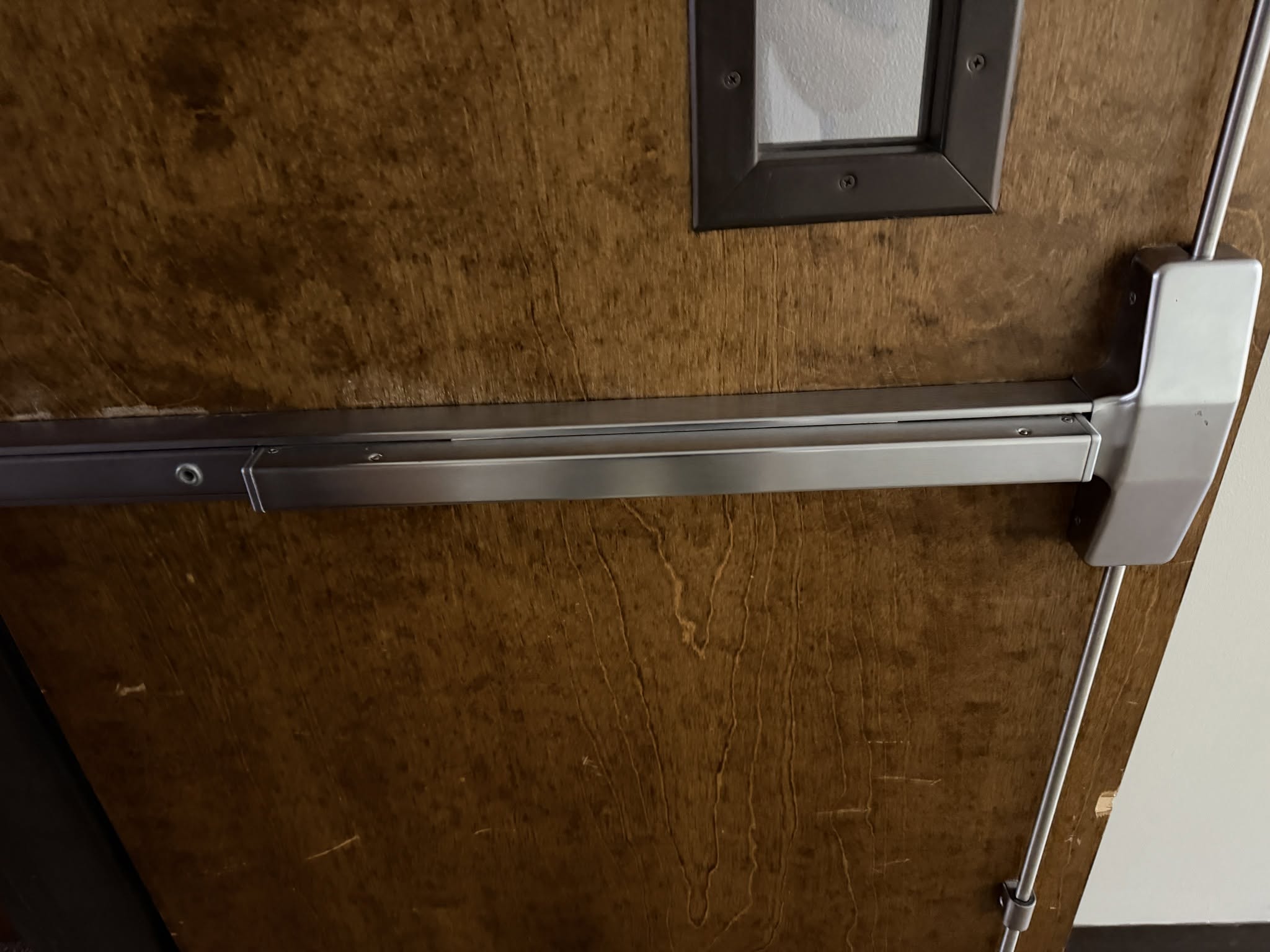 Close-up of a wooden door with a silver push bar and small window.