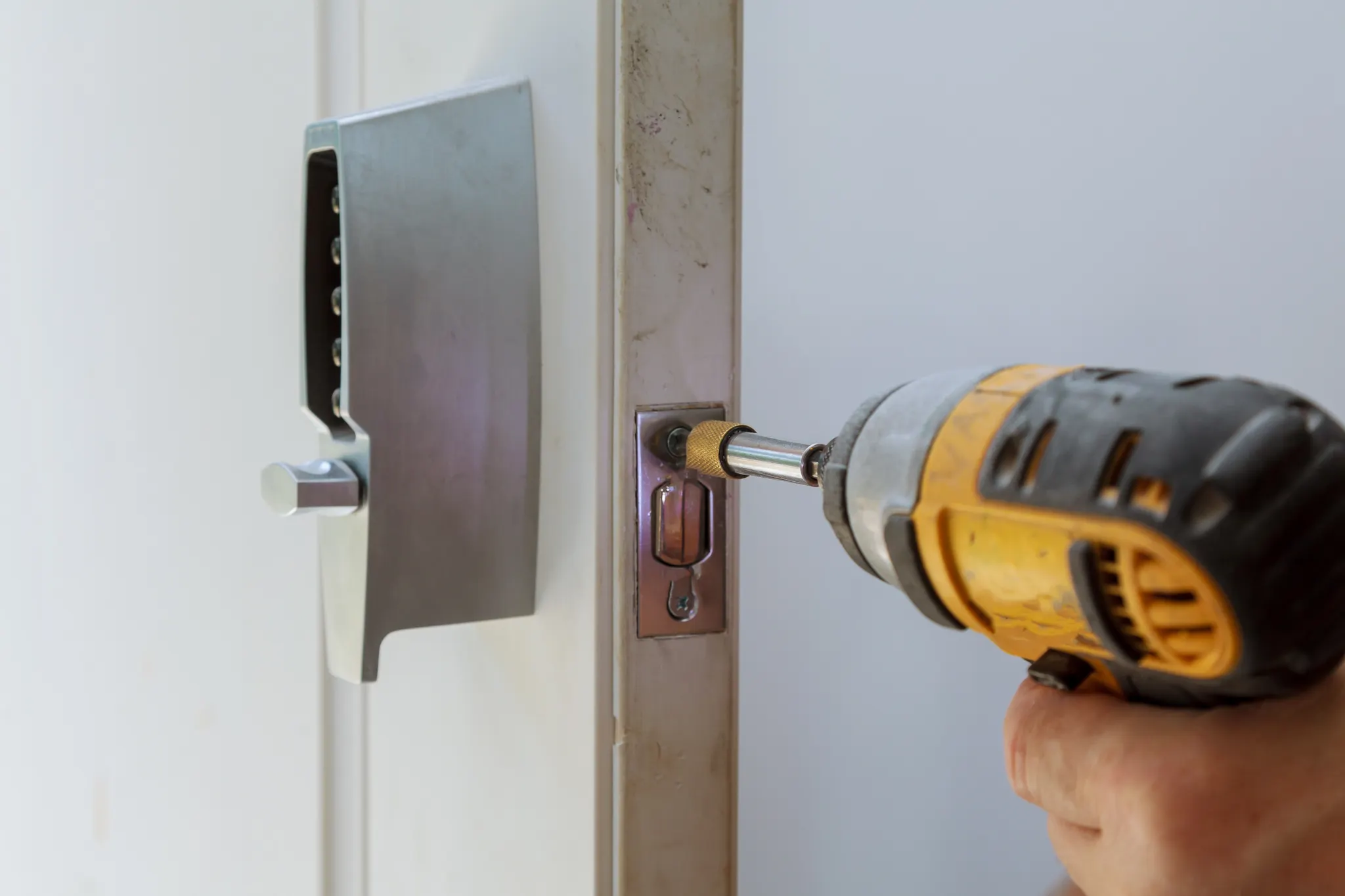 Close-up of a person using a power drill to install a door lock.