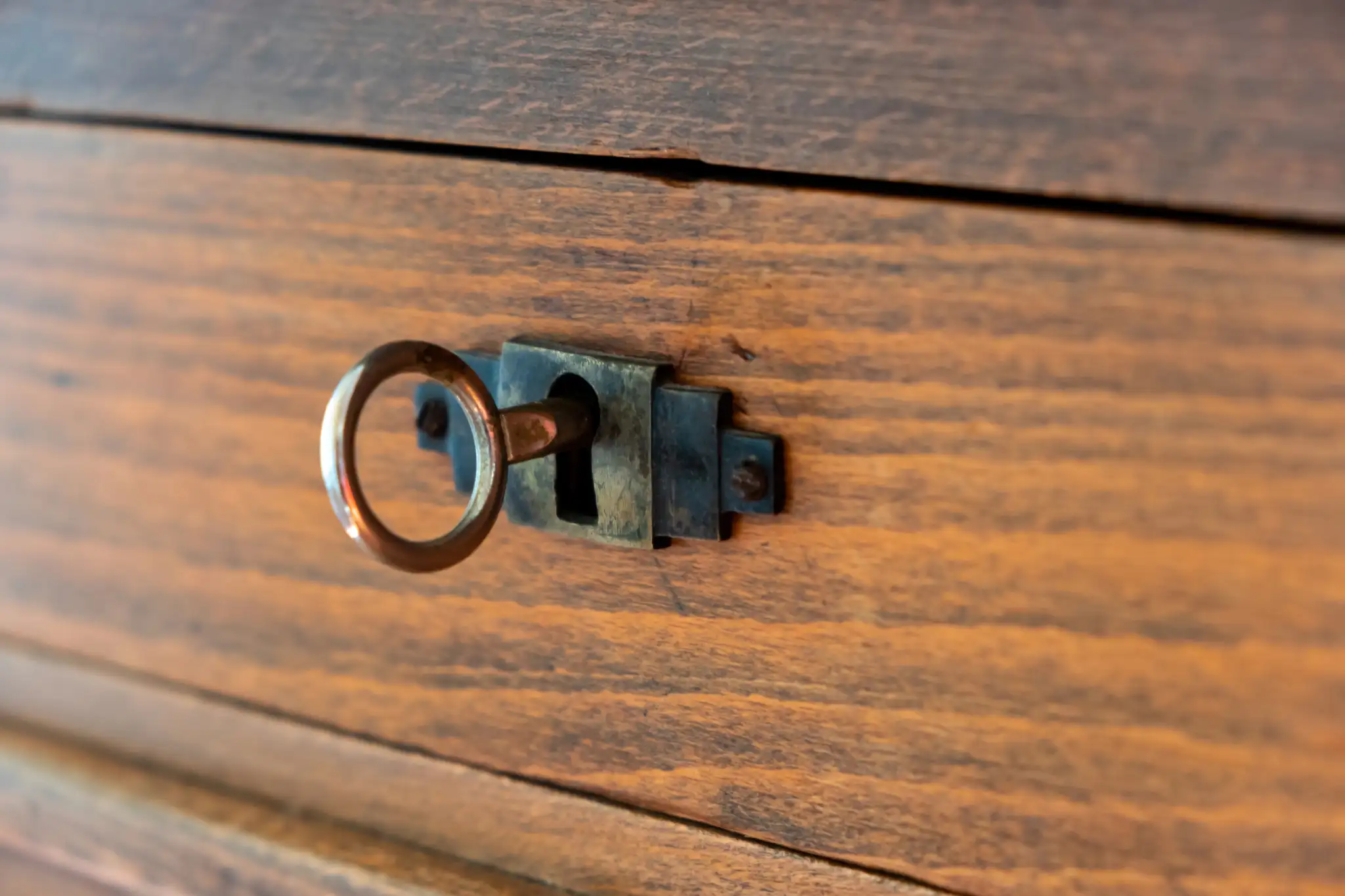 Close-up of a brass key in an old wooden drawer's lock.