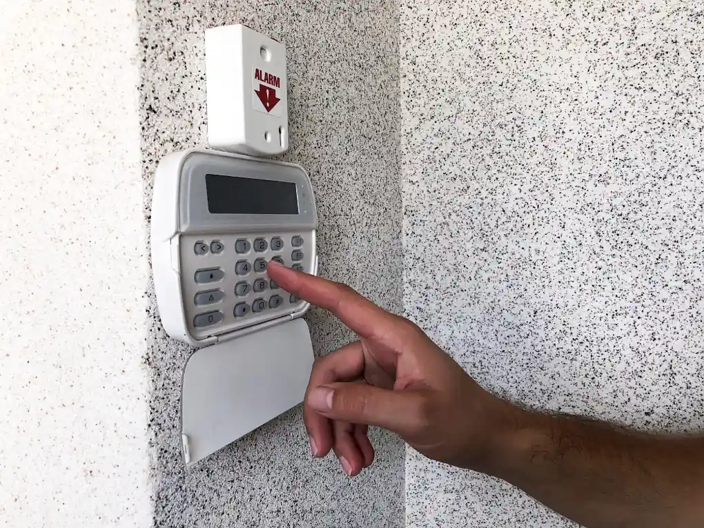 A hand entering a code on a white security alarm keypad.