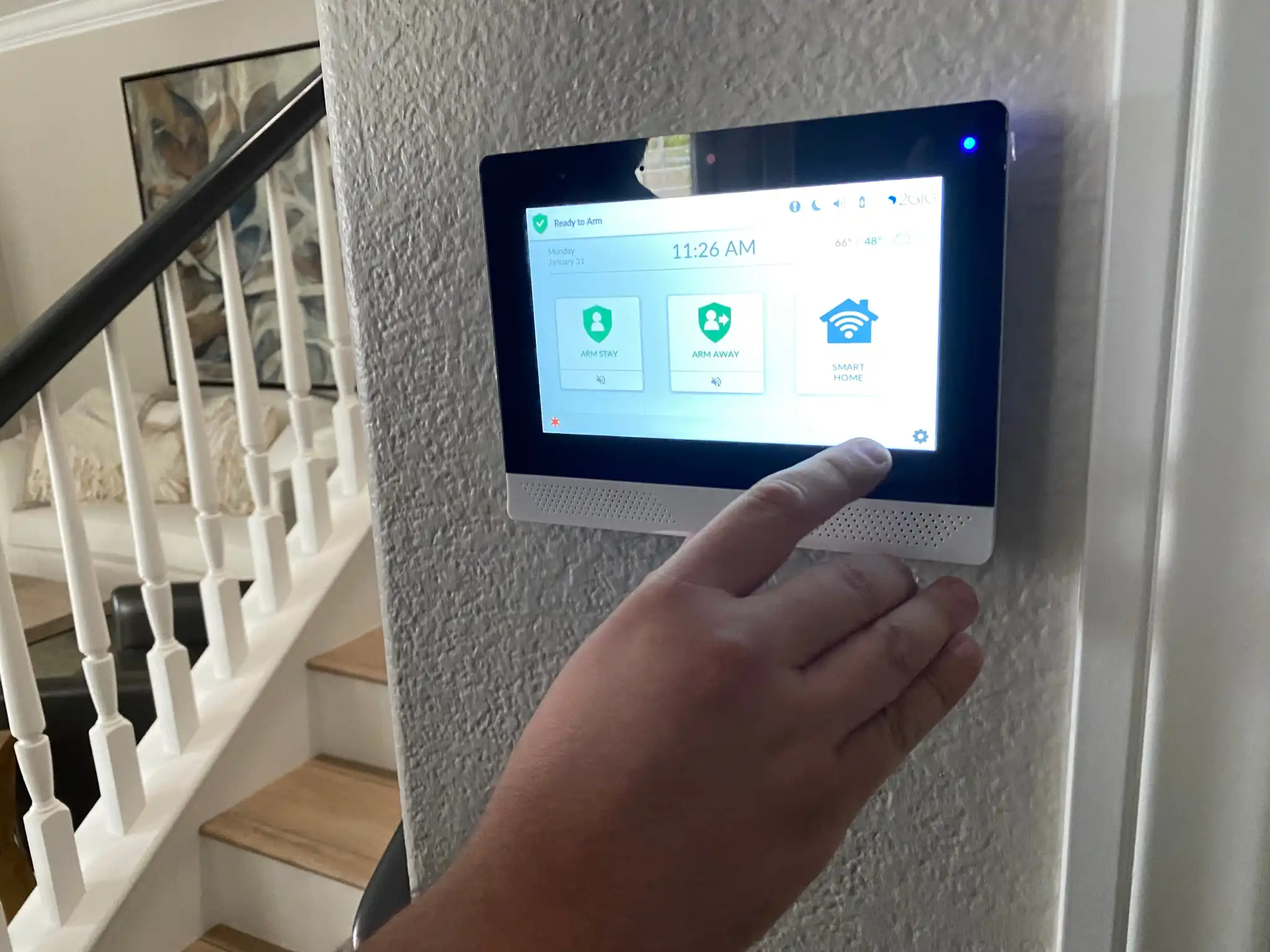 Hand touching a smart home security panel mounted on a wall.