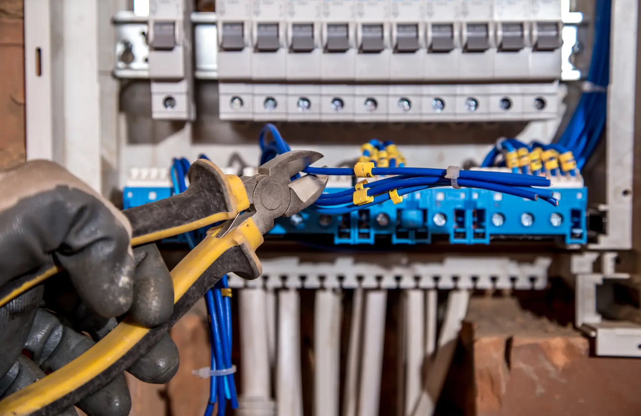 Hand in glove cutting blue wires in an electrical panel