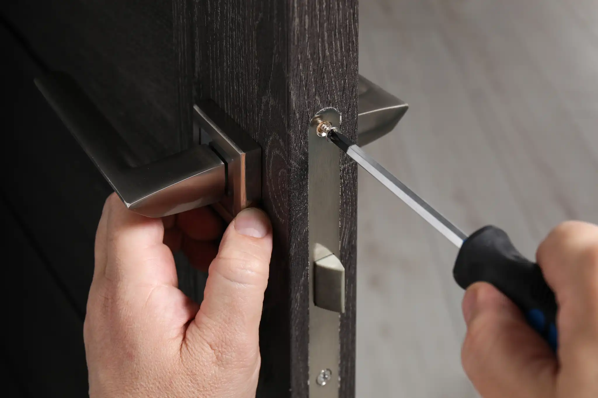Close-up of hands installing a door handle with a screwdriver