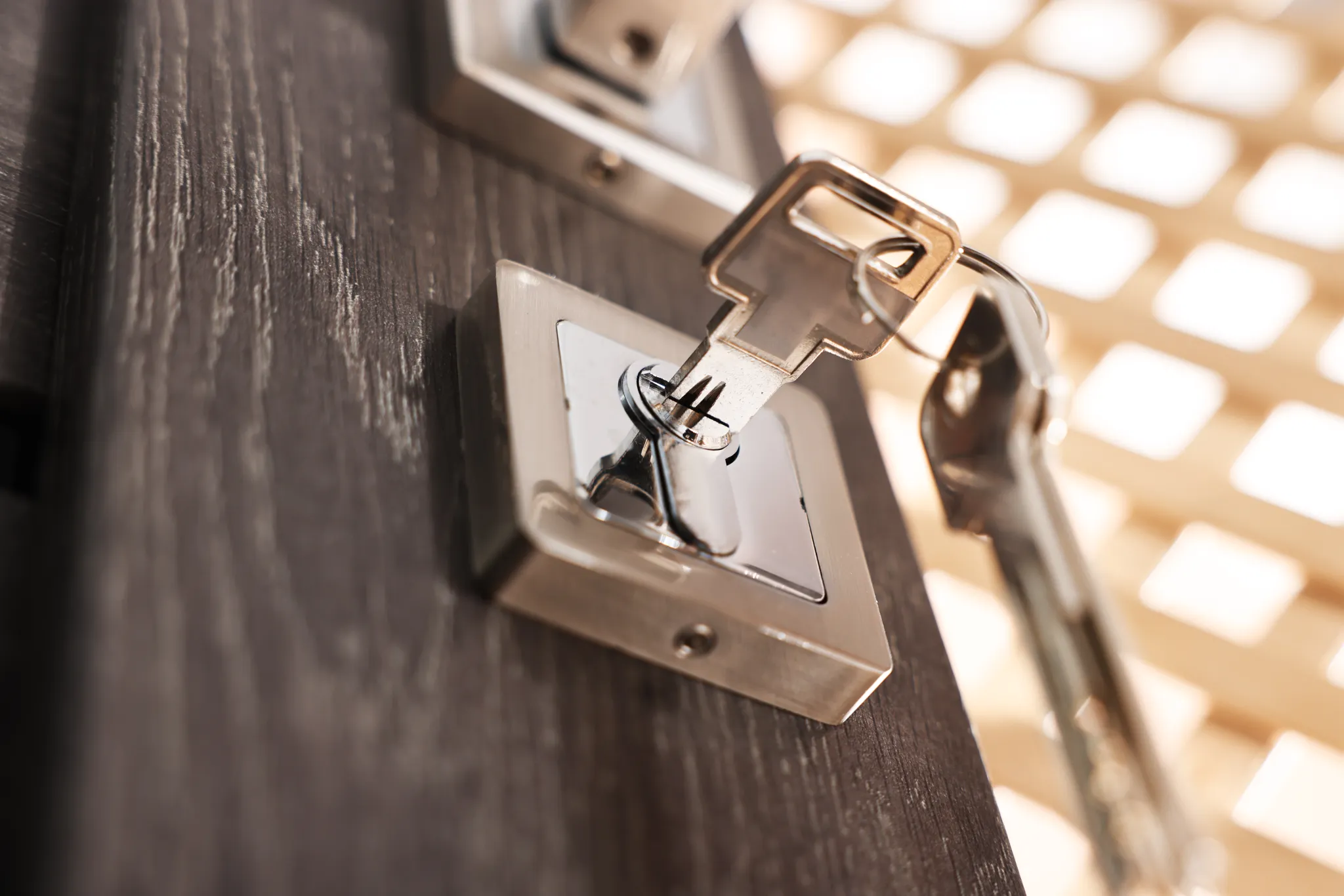 Close-up of a silver key in a door lock on a dark wooden door.